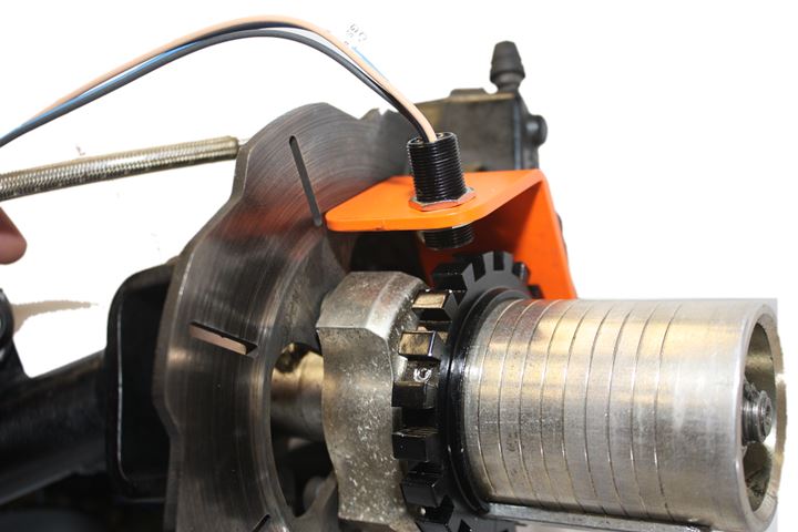 Inductive wheel-speed sensor on an orange bracket above a toothed ring next to the brake disc